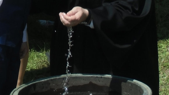 Pastor Nagel tauft mit Wasser aus dem großen Waschbottich